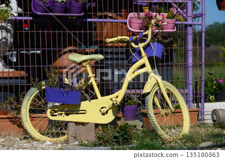 Charming yellow bicycle adorned with blooming flowers beside a colorful garden in a sunny countryside setting Charming yellow bicycle adorned with blooming flowers beside a colorful garden in a sunny countryside setting 135180863