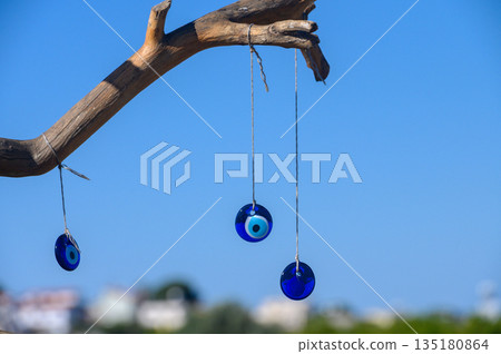 Beautiful blue talismans swinging gently from a branch under a clear sky in a serene coastal setting Beautiful blue talismans swinging gently from a branch under a clear sky in a serene coastal setting 135180864