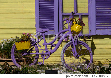 Colorful bicycle adorned with flowers brightens up a cheerful yellow building on a sunny day in a vibrant neighborhood Colorful bicycle adorned with flowers brightens up a cheerful yellow building on a sunny day in a vibrant neighborhood 135180867