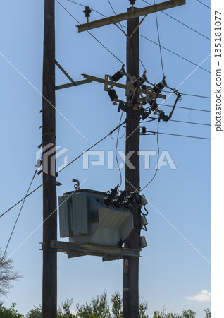 High above the ground, power lines and equipment connect the urban landscape on a clear sunny day in a rural setting 135181077