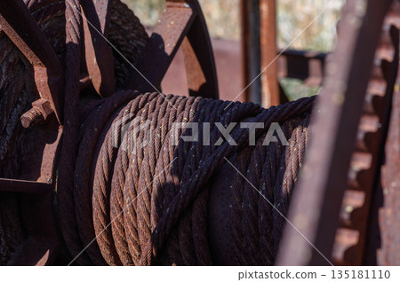 Rusty gears and worn ropes tell tales of a forgotten mining era in a serene desert landscape at sunset 135181110