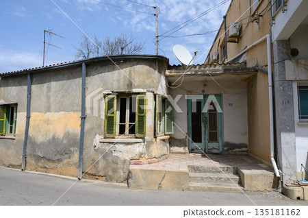 Weathered house with green shutters on a quiet street under a cloudy sky during midday 135181162