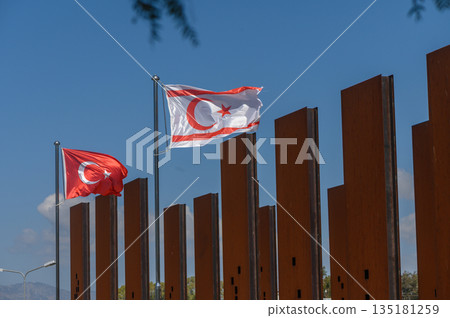 Waving flags of Turkey and Northern Cyprus celebrate unity against a backdrop of a blue sky and modern architecture 135181259