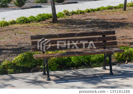 Wooden bench nestled among greenery in a tranquil park setting, inviting moments of relaxation and reflection Wooden bench nestled among greenery in a tranquil park setting, inviting moments of relaxation and reflection 135181288