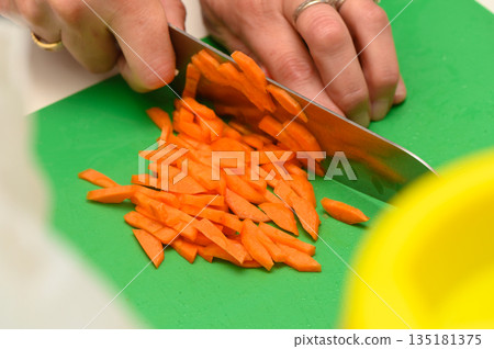 Slicing fresh carrots with precision in a cheerful kitchen during a sunny afternoon cooking session 135181375