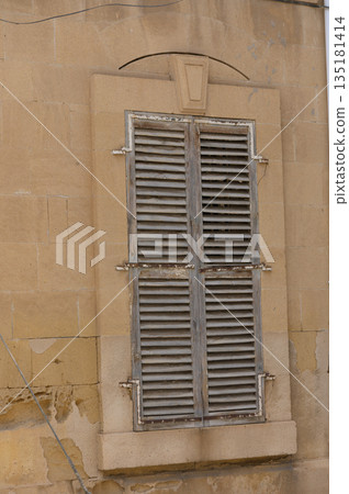 Old wooden shutters on a weathered stone wall hint at stories of a time long forgotten in a quaint historical town 135181414