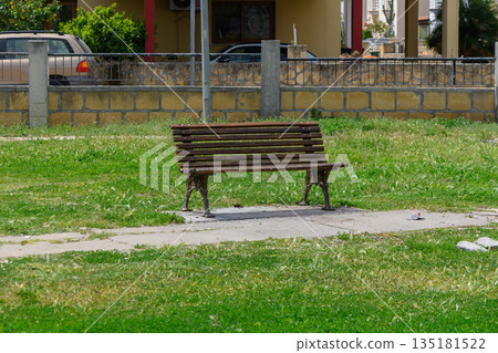 Empty wooden bench in a sunlit park surrounded by lush green grass inviting moments of tranquility 135181522