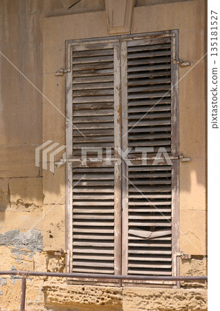 Weathered wooden shutters on a rustic wall reveal the charm of an old building in a coastal town 135181527