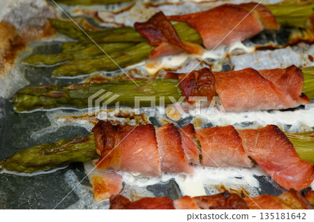 Savory asparagus wrapped in crispy bacon sizzling on a baking sheet in a cozy kitchen setting Savory asparagus wrapped in crispy bacon sizzling on a baking sheet in a cozy kitchen setting 135181642