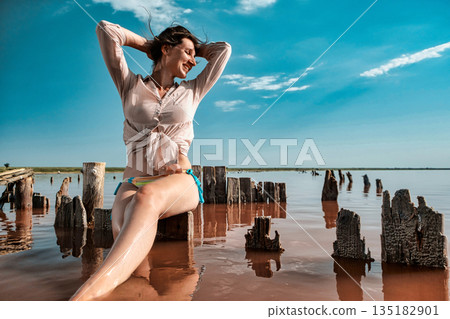 Woman in a white pink shirt posing on the pink lake and blue sky. Beautiful happy girl smiling download Woman in a white pink shirt posing on the pink lake and blue sky. Beautiful happy girl smiling download 135182901