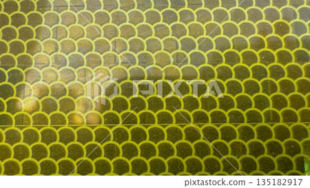 Close-up of yellow reflective vinyl film with a repeating scales pattern. Close-up of yellow reflective vinyl film with a repeating scales pattern. 135182917