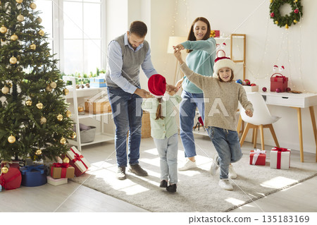 Joyful family celebrating Christmas together, dancing near tree and enjoying festive holiday spirit. Joyful family celebrating Christmas together, dancing near tree and enjoying festive holiday spirit. 135183169
