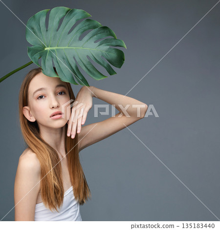 Young caucasian female with monstera leaf posing stylishly against gray Young caucasian female with monstera leaf posing stylishly against gray 135183440