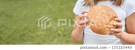 Female teen holding fresh round bread outdoors in green grass background 135183449