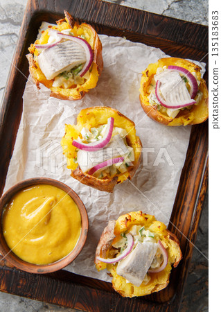 Homemade baked potato cups stuffed with egg salad and salted herring served with mustard sauce close-up on a wooden board on the table. Vertical top view 135183683