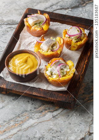 Scandinavian-style baked potatoes stuffed with salad and herring fillet close-up on a wooden board. Vertical 135183687