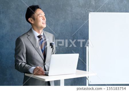 A man giving a presentation wearing a lapel microphone in front of a whiteboard A man giving a presentation wearing a lapel microphone in front of a whiteboard 135183754