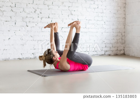 Fit Caucasian woman practice Ananda Balasana exercise indoor in loft studio. Happy Baby Pose, yoga. Fit Caucasian woman practice Ananda Balasana exercise indoor in loft studio. Happy Baby Pose, yoga. 135183803