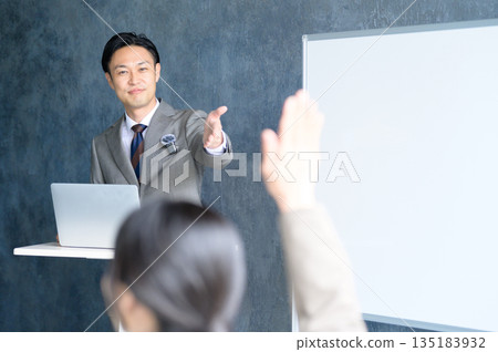 A Japanese man giving a presentation using a lapel microphone in front of a whiteboard A Japanese man giving a presentation using a lapel microphone in front of a whiteboard 135183932