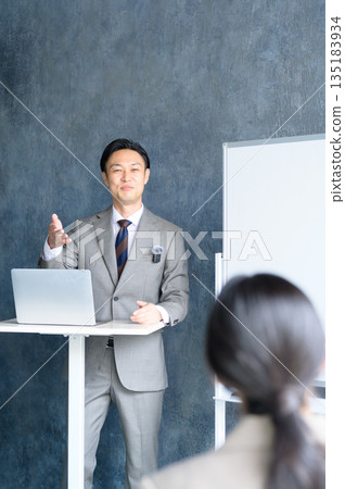 A Japanese man giving a presentation using a lapel microphone in front of a whiteboard A Japanese man giving a presentation using a lapel microphone in front of a whiteboard 135183934