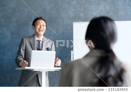 A Japanese man giving a presentation using a lapel microphone in front of a whiteboard A Japanese man giving a presentation using a lapel microphone in front of a whiteboard 135183935