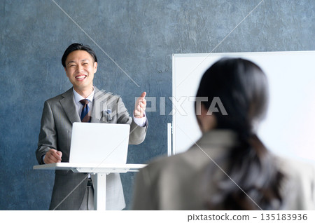 A Japanese man giving a presentation using a lapel microphone in front of a whiteboard A Japanese man giving a presentation using a lapel microphone in front of a whiteboard 135183936