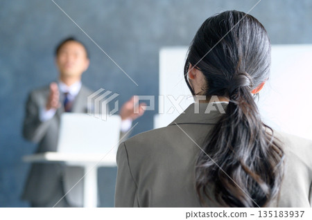 A Japanese man giving a presentation using a lapel microphone in front of a whiteboard 135183937