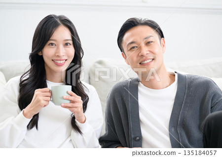 A man and woman relaxing in front of a sofa in the living room with mugs A man and woman relaxing in front of a sofa in the living room with mugs 135184057