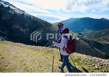 Two Hikers With Backpacks Trekking Along Mountain Trail With Scenic Valley 135184094