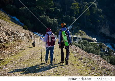 Two Hikers With Backpacks Trek Mountain Trail With Dog In Rocky Landscape 135184097