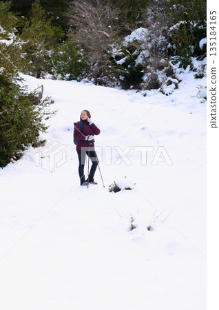 Woman Hiking in Snowy Forest Trail With Trekking Poles and Backpack 135184165