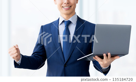 一名手持電腦的男性商人揮拳慶祝。 一名手持電腦的男性商人揮拳慶祝。 135184720