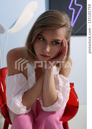 Female model seated with neon logo behind in stylish boutique ambiance Female model seated with neon logo behind in stylish boutique ambiance 135185759