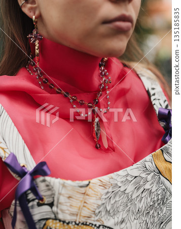 stylist accessorizing layered necklaces over red turtleneck 135185835
