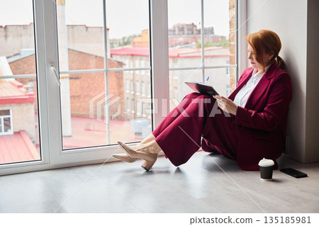 Person dressed in burgundy focusing on business notes and future plans 135185981