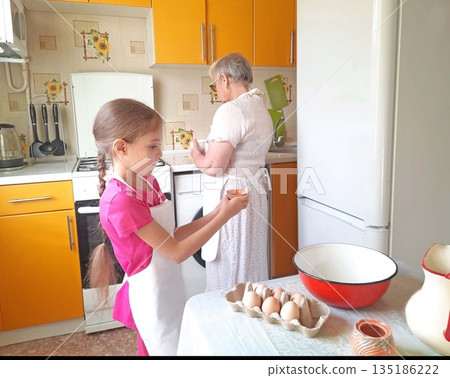 A grandmother and her granddaughter set out the necessary ingredients for cooking on the table. 135186222