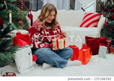 Merry Christmas, Happy Holidays banner. Cheerful pretty young 30s woman in red sweater having got a Christmas presents and sit on the floor near sofa and decorated Christmas tree. Full body Merry Christmas, Happy Holidays banner. Cheerful pretty young 30s woman in red sweater having got a Christmas presents and sit on the floor near sofa and decorated Christmas tree. Full body 135186392
