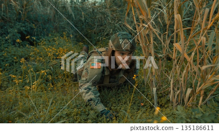 A soldier crawls on the ground in a meadow to better observe the enemy A soldier crawls on the ground in a meadow to better observe the enemy 135186611