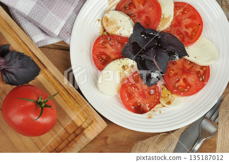 Caprese salad - tomatoes, basil and mozzarella cheese on a wooden background 135187012