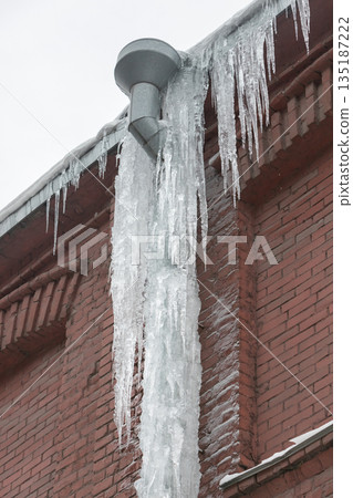 Closeup of drainpipe of building covered with thick layer of ice and icicles Closeup of drainpipe of building covered with thick layer of ice and icicles 135187222