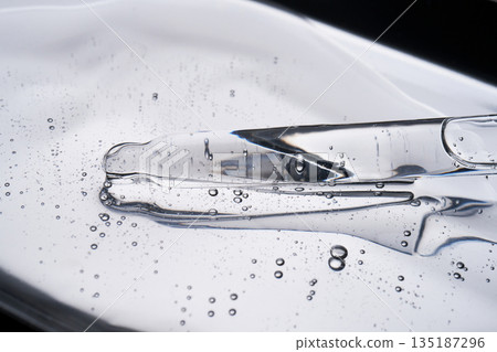 Glass pipette dispensing clear hydrating serum on a shiny surface Glass pipette dispensing clear hydrating serum on a shiny surface 135187296