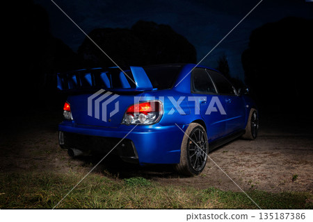 Sleek blue sports car in night backdoor behind. Sleek blue sports car in night backdoor behind. 135187386