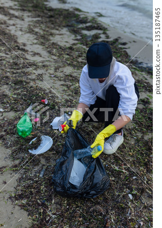 Volunteer collecting plastic waste during beach cleanup, removing litter and protecting the shoreline environment. Volunteer collecting plastic waste during beach cleanup, removing litter and protecting the shoreline environment. 135187465