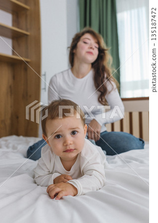 Young mother playing with her baby at home, enjoying a warm and cozy family moment full of tenderness, comfort, natural light, and playful parent-child connection. 135187472
