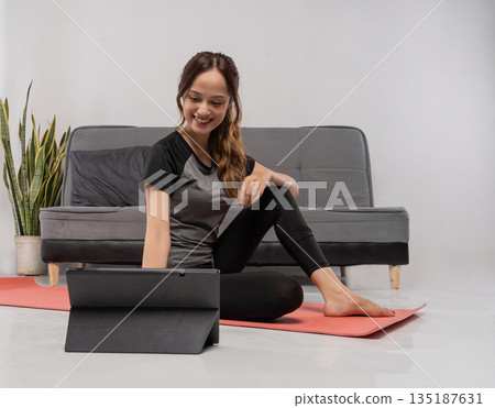 Female engaged in workout while watching tablet comfortably Female engaged in workout while watching tablet comfortably 135187631