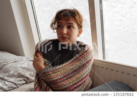 young woman warms herself near radiator at home in winter weather. young woman warms herself near radiator at home in winter weather. 135187682