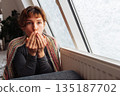 young woman warms herself near radiator at home in winter weather. 135187702