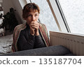 young woman warms herself near radiator at home in winter weather. 135187704