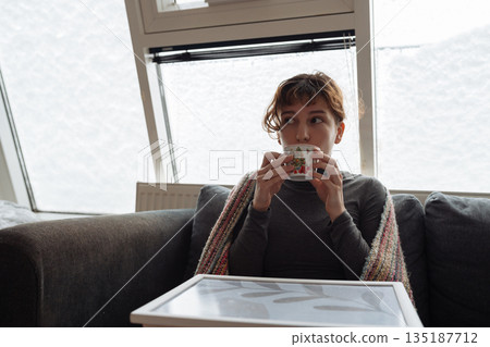 young woman warms up with hot tea in winter weather at home 135187712