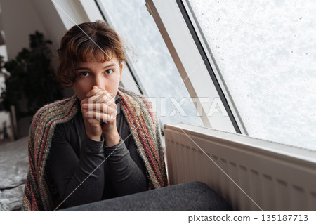 young woman warms herself near radiator at home in winter weather. 135187713